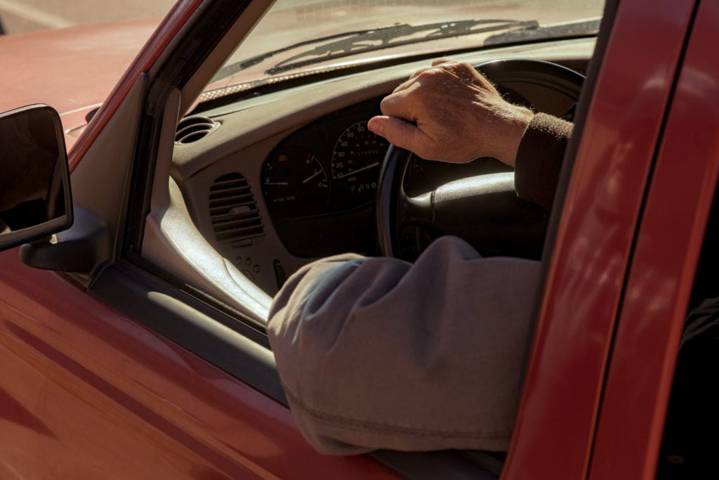 A man hangs his elbow out the window of his red pickup truck as he drives through OneGenAway's mobile pantry to receive food.