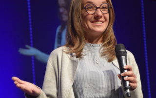 Daelyn Houser speaks on stage at OneGenAway's Million Meal Spring Breakfast in Alabama.