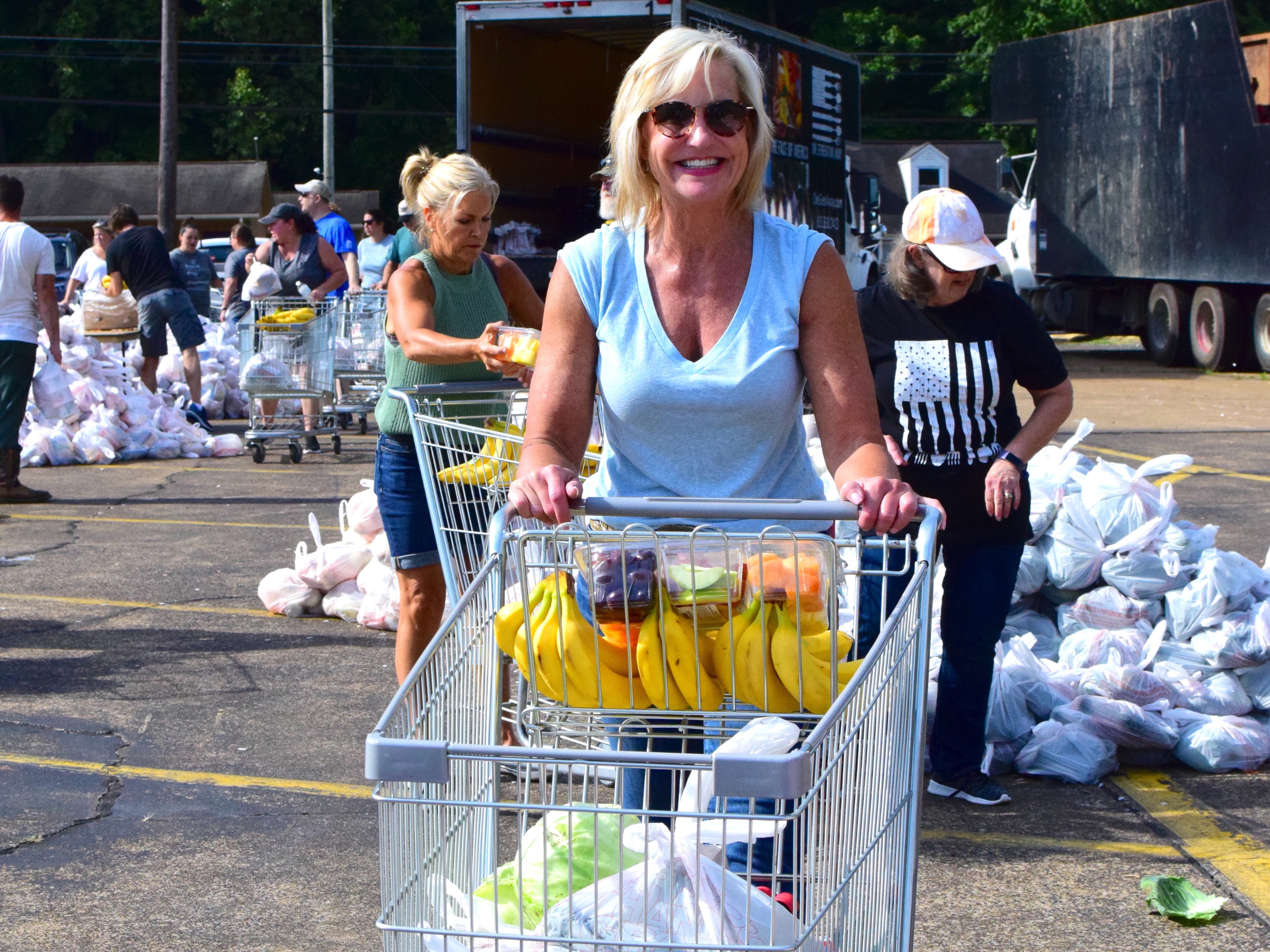 Woman volunteering at the OneGenAway Mobile Pantry pushes a shopping cart filled with groceries, including bananas and other produce.