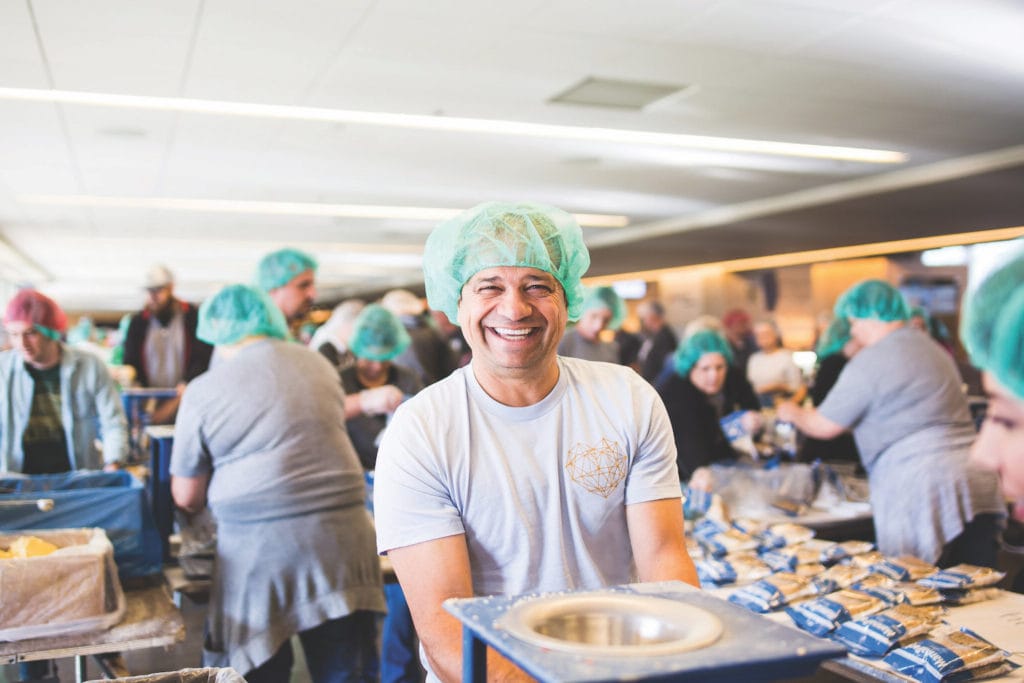 A man in a blue hairnet packs food for families overseas at a Feed My Starving Children MobilePack event.
